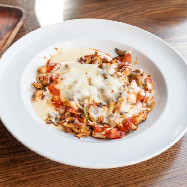 Chicken fajitas with melted cheese and red sauce in a white bowl on a wooden table.