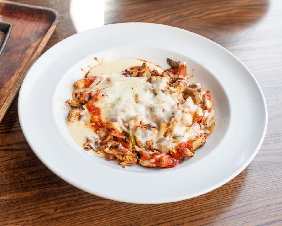 Chicken fajitas with melted cheese and red sauce in a white bowl on a wooden table.
