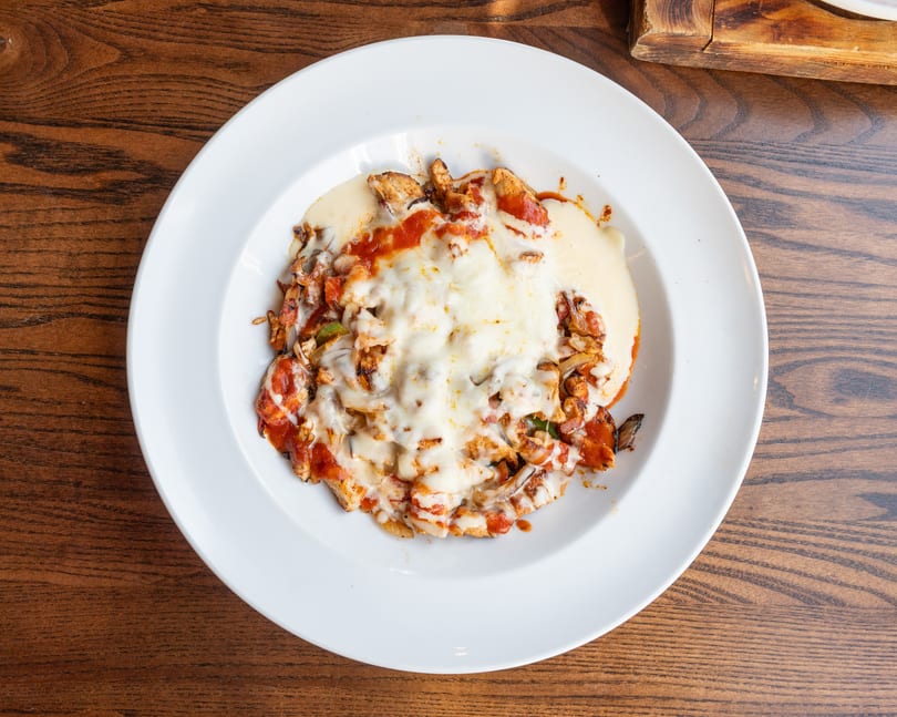 Chicken fajitas with melted cheese and red sauce on a white plate.