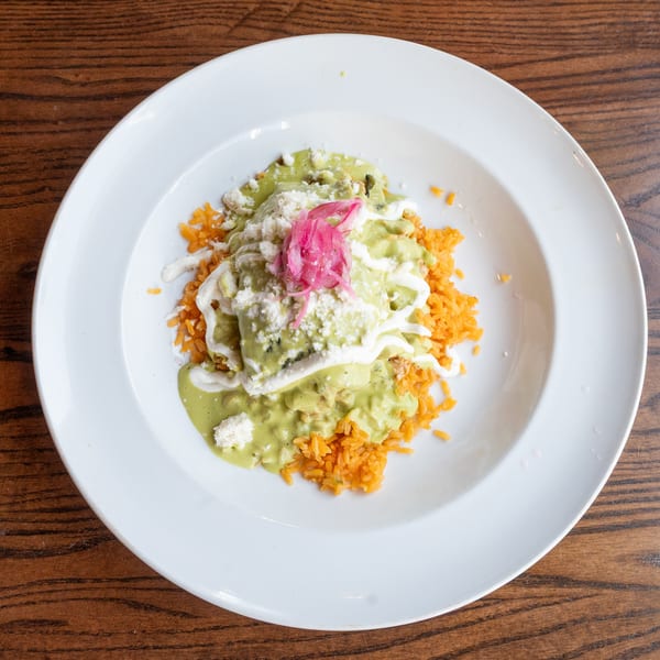 Enchiladas with green sauce, white cheese, and pickled red onions, served with orange rice.