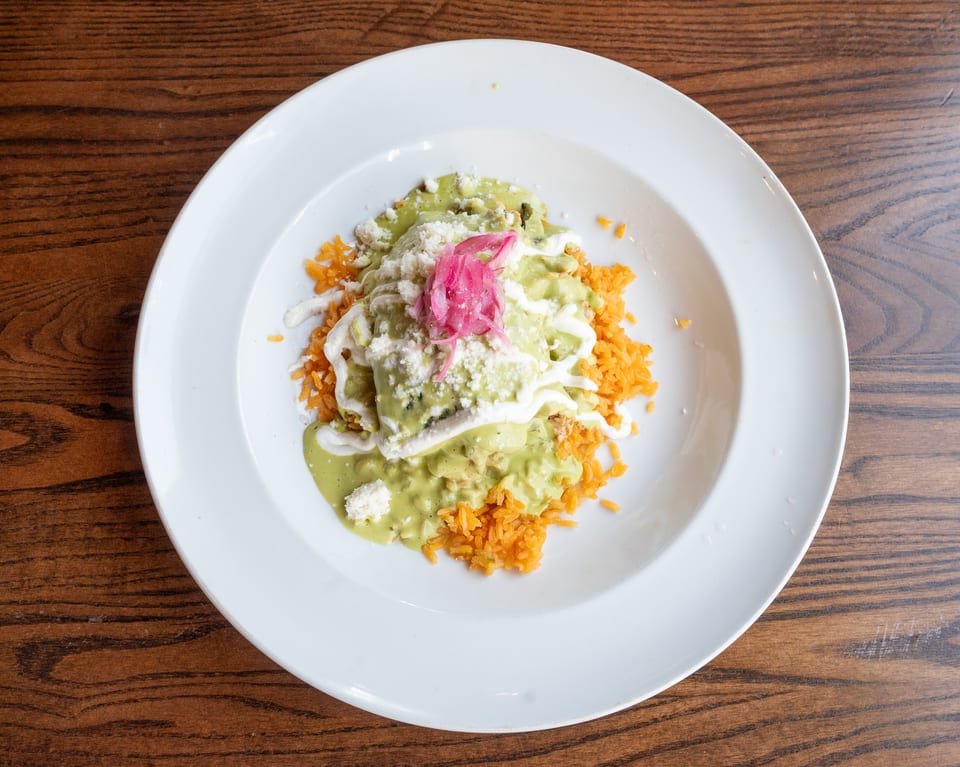 Enchiladas with green sauce, white cheese, and pickled red onions, served with orange rice.