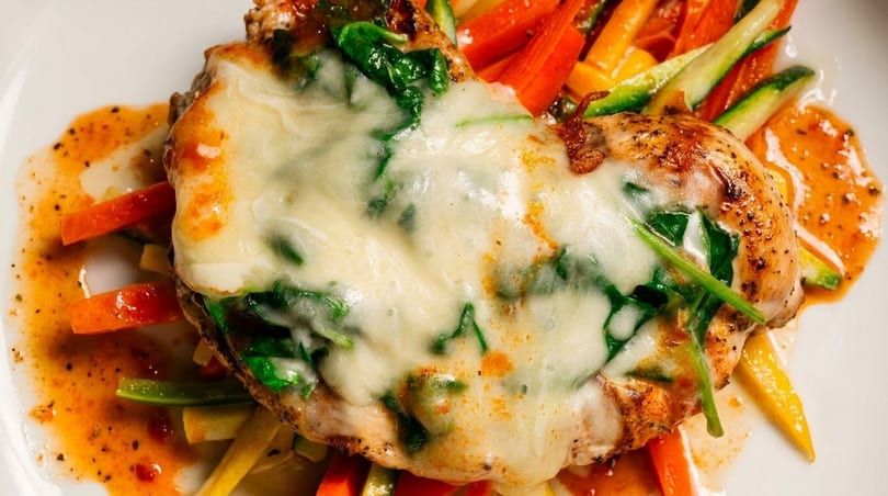 Chicken breast topped with melted cheese and spinach, served with colorful julienned vegetables and sauce.