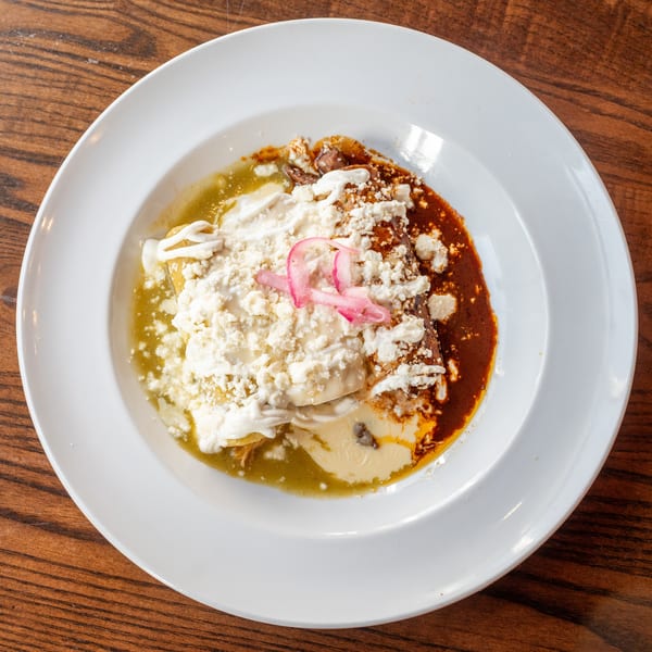 A plate of enchiladas with green and red sauce, topped with cheese, sour cream, and pickled onions.