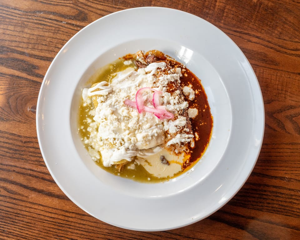 A plate of enchiladas with green and red sauce, topped with cheese, sour cream, and pickled onions.