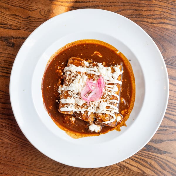 Three enchiladas covered in rich mole sauce, crumbled cheese, crema, and pickled red onions.