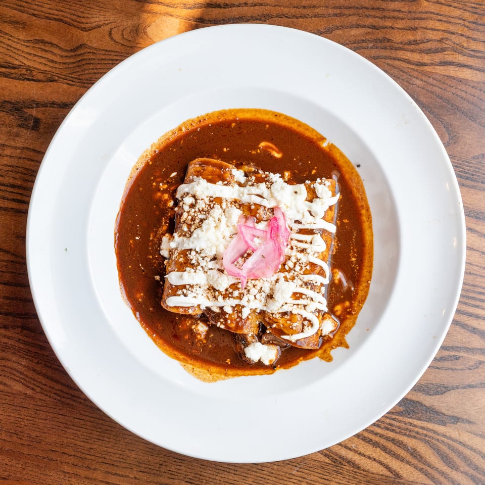 Three enchiladas covered in rich mole sauce, crumbled cheese, crema, and pickled red onions.