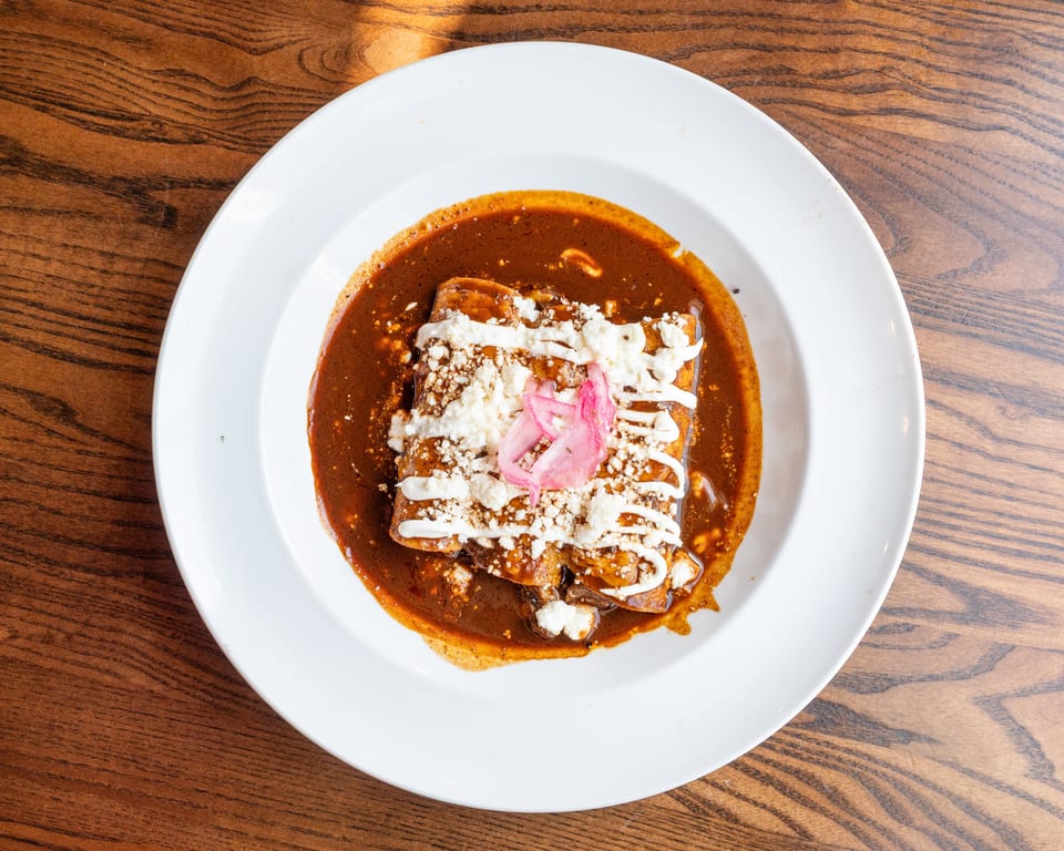 Three enchiladas covered in rich mole sauce, crumbled cheese, crema, and pickled red onions.